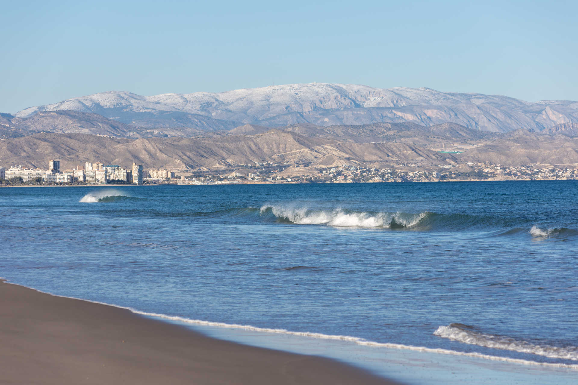 The waves of Playa de Sant Joan with the mountains in the background.