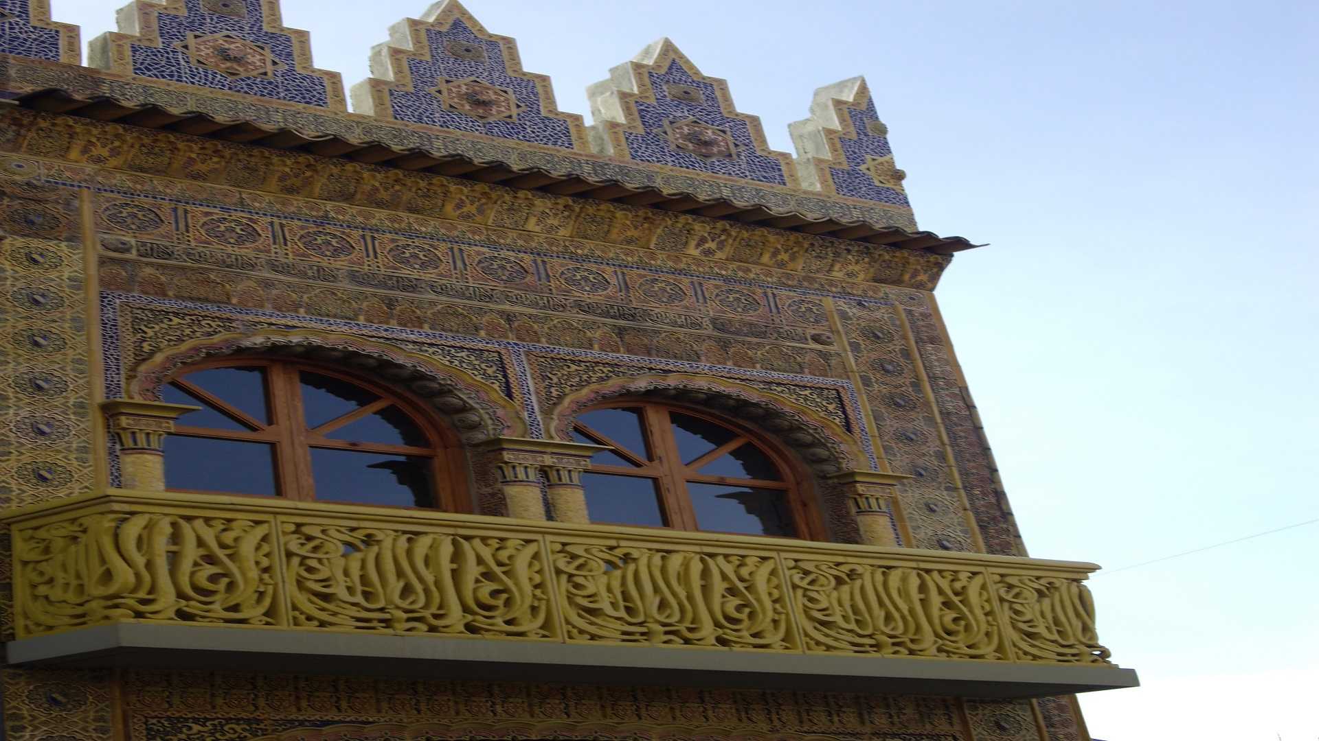 Parte superior del segundo cuerpo de la fachada de El Arte donde se ve la imagen de un balcón con dos ventanas, en colores amarillo y azul, de estilo hispano-árabe, inspirado en las yeserías de la Alhambra.  